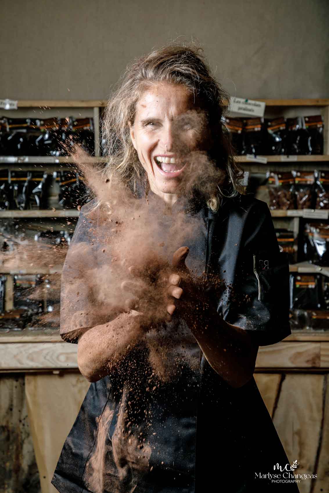 A chocolate maker bursts out laughing in a cloud of cocoa powder
