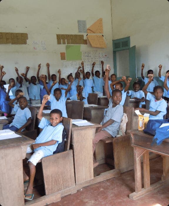 Schoolchildren in blue smocks in São Tomé, hands raised in their classroom