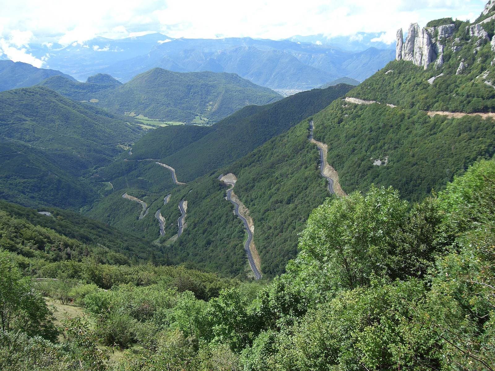 Looking down from the Col de Rousset onto the hairpins of the road winding towards the Die valley, between wooded slopes and limestone pinnacles.