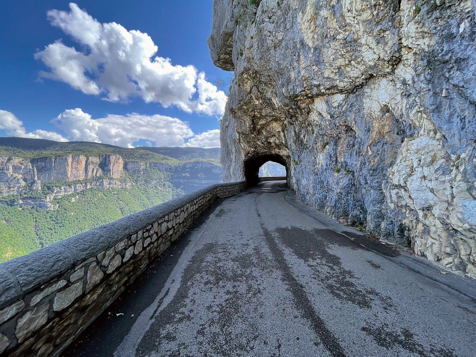 The Combe Laval road cut into the cliff, with its stone parapet and a tunnel hewn through the rock above the drop.
