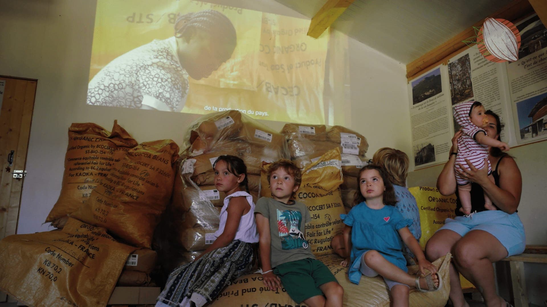 Enfants assis sur des sacs de fèves de cacao bio, devant la projection d’un film sur São Tomé